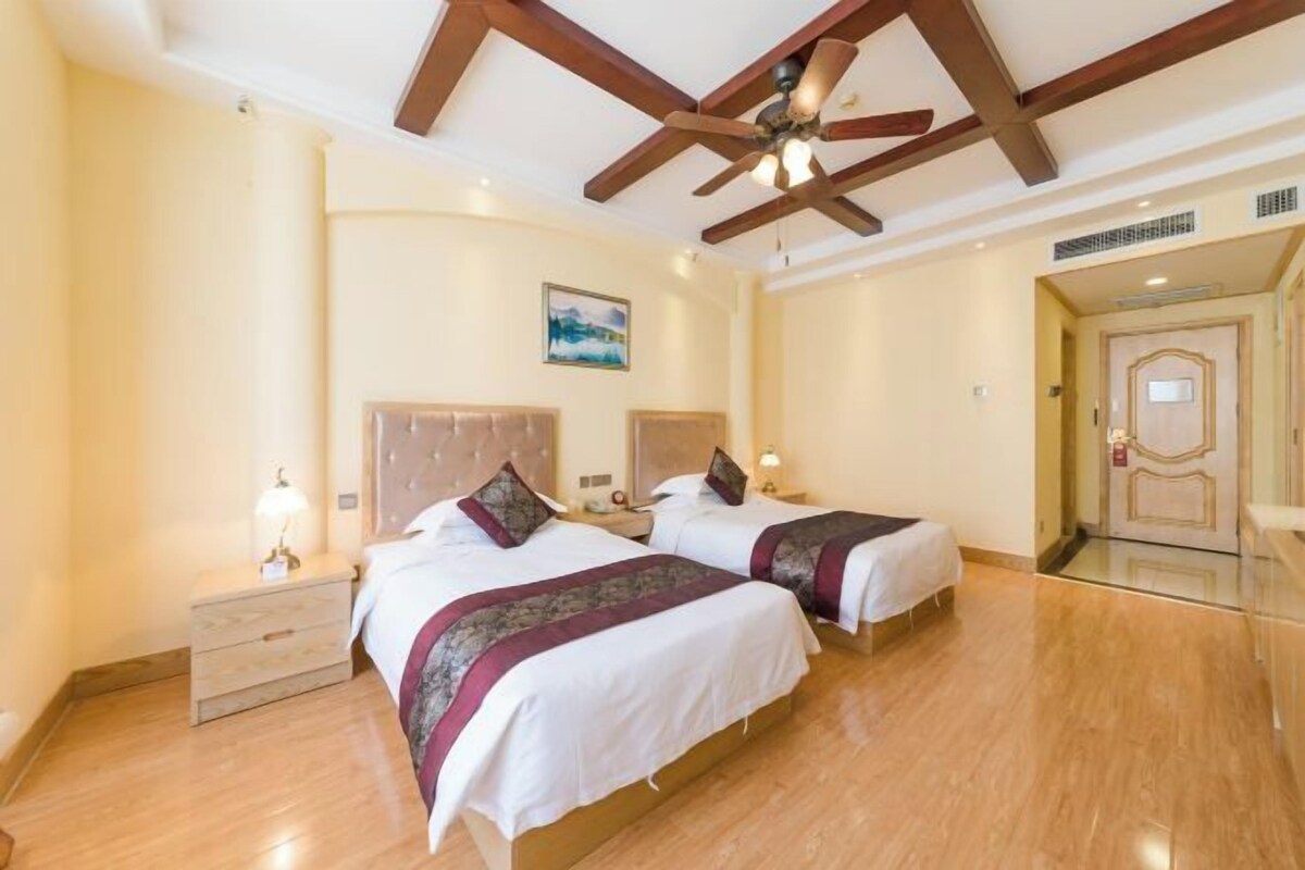 Habitación de hotel con dos camas, suelo de madera, ventilador de techo y un cuadro en la pared.