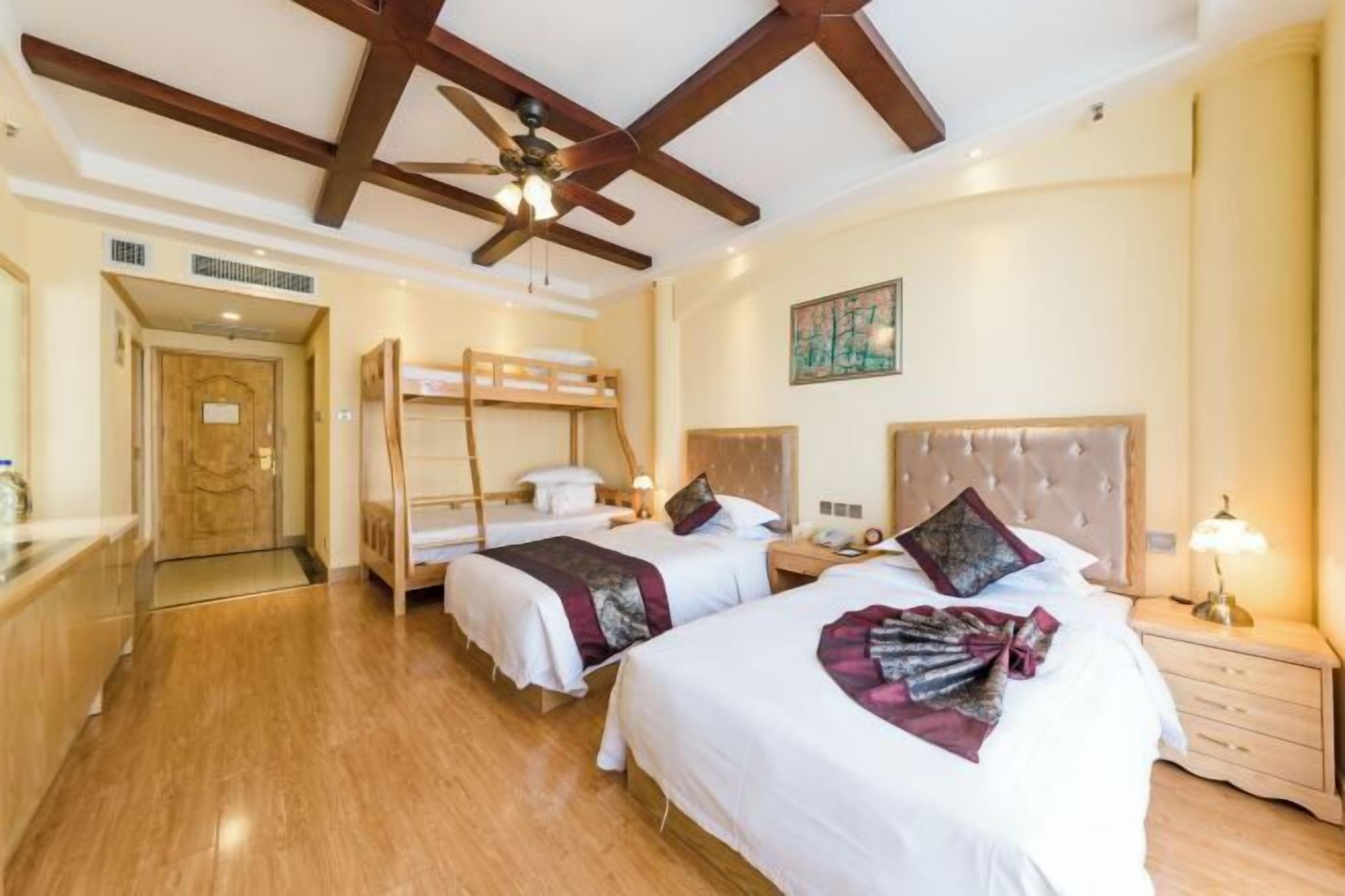Ein Hotelzimmer mit zwei Betten, einem Deckenventilator, einem Bild an der Wand und Holzboden.