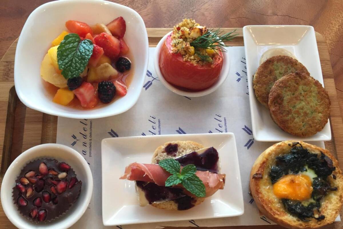 A tray with various food items including a bowl of mixed fruits, a stuffed tomato, two small patties, a chocolate dessert, and a sandwich.