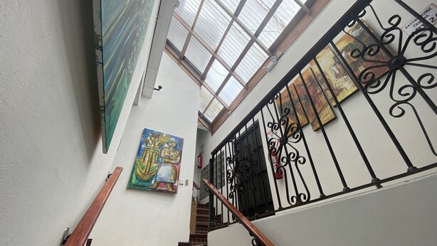 A staircase with a wooden handrail and black wrought iron balusters, leading to a landing with a glass ceiling and a painting on the wall.
