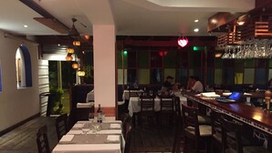 A restaurant with multiple tables and chairs, a bar area with a laptop, and a view of the street outside.