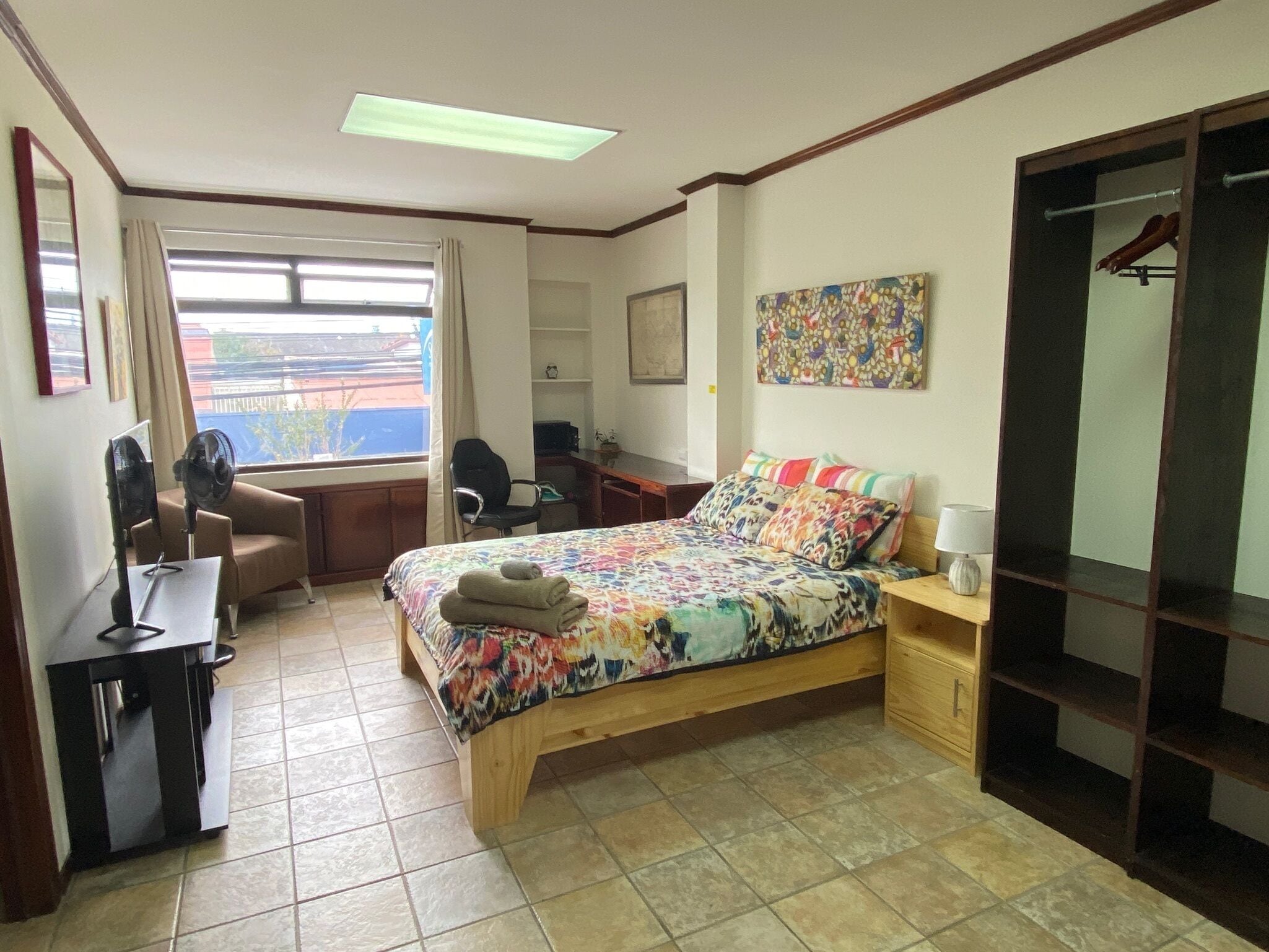 A bedroom with a bed, desk, chair, and a window with curtains.