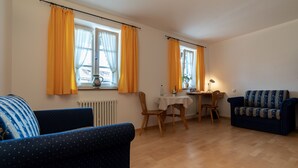 Una sala de estar con dos sofás, una mesa de comedor con sillas y ventanas grandes con cortinas amarillas.