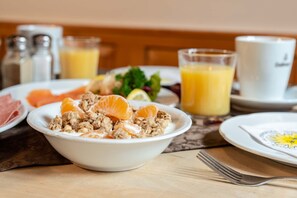 Une table mise pour le petit-déjeuner avec un bol de céréales, des tranches d’orange et un verre de jus d’orange.