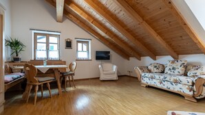 Acogedor dormitorio en ático con vigas de madera, una mesa de comedor con sillas, un sofá y un televisor.