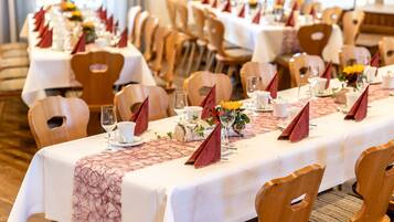 A banquet hall with long tables set for a formal event, featuring white tablecloths, wooden chairs, and red napkins.
