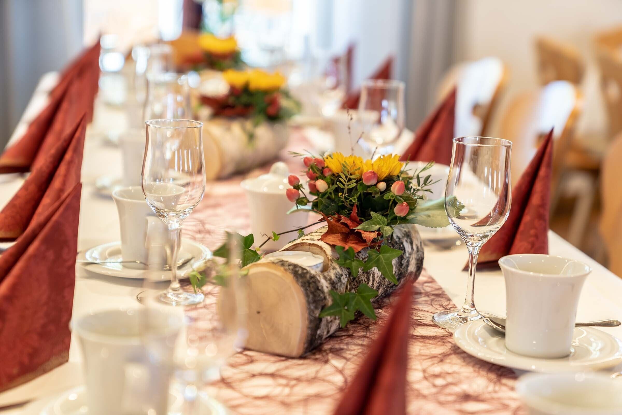A dining table set with white plates, clear glasses, and red napkins.