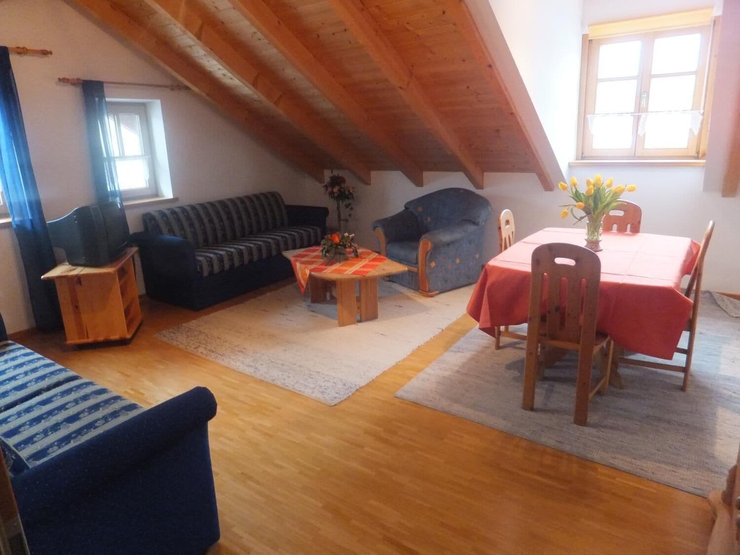 Ein gemütlicher Loftsraum mit Holzboden, einer Couch, einem Esstisch mit Stühlen und einem kleinen Beistelltisch.