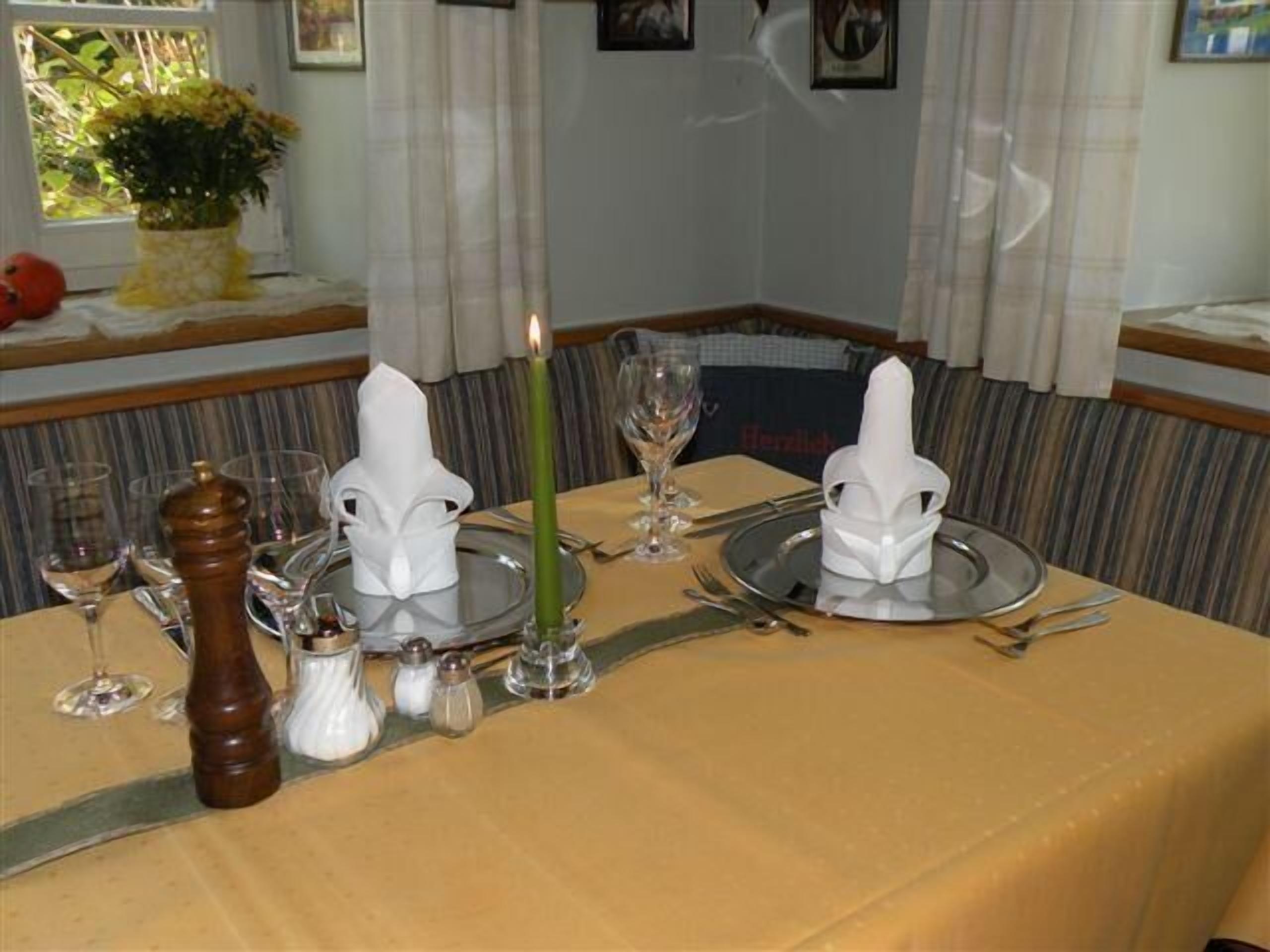 A dining table set with white napkins, a green candle, wine glasses, and salt and pepper shakers.