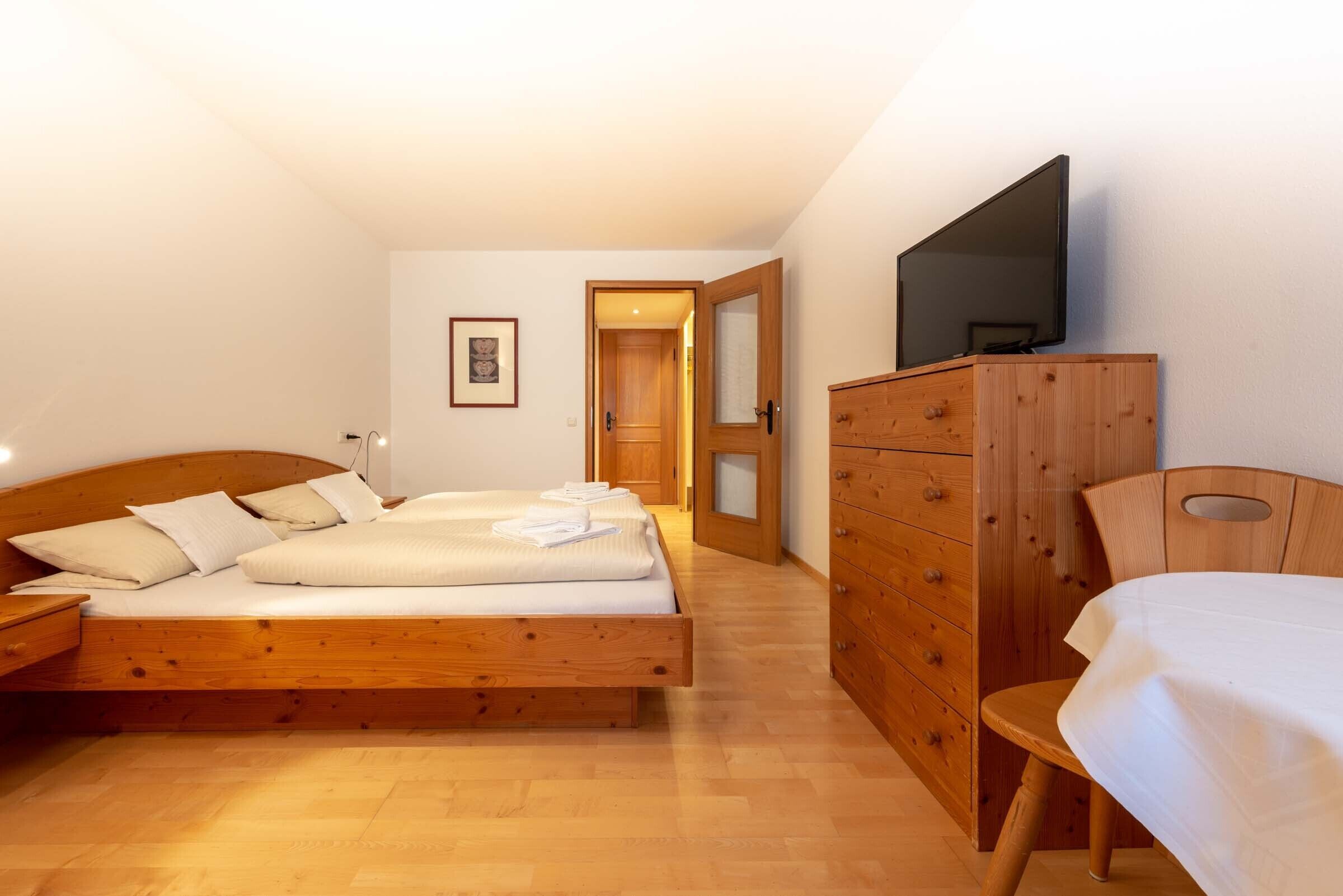 Un dormitorio con cama de madera, cómoda, televisor en la pared y una puerta que da a otra habitación.