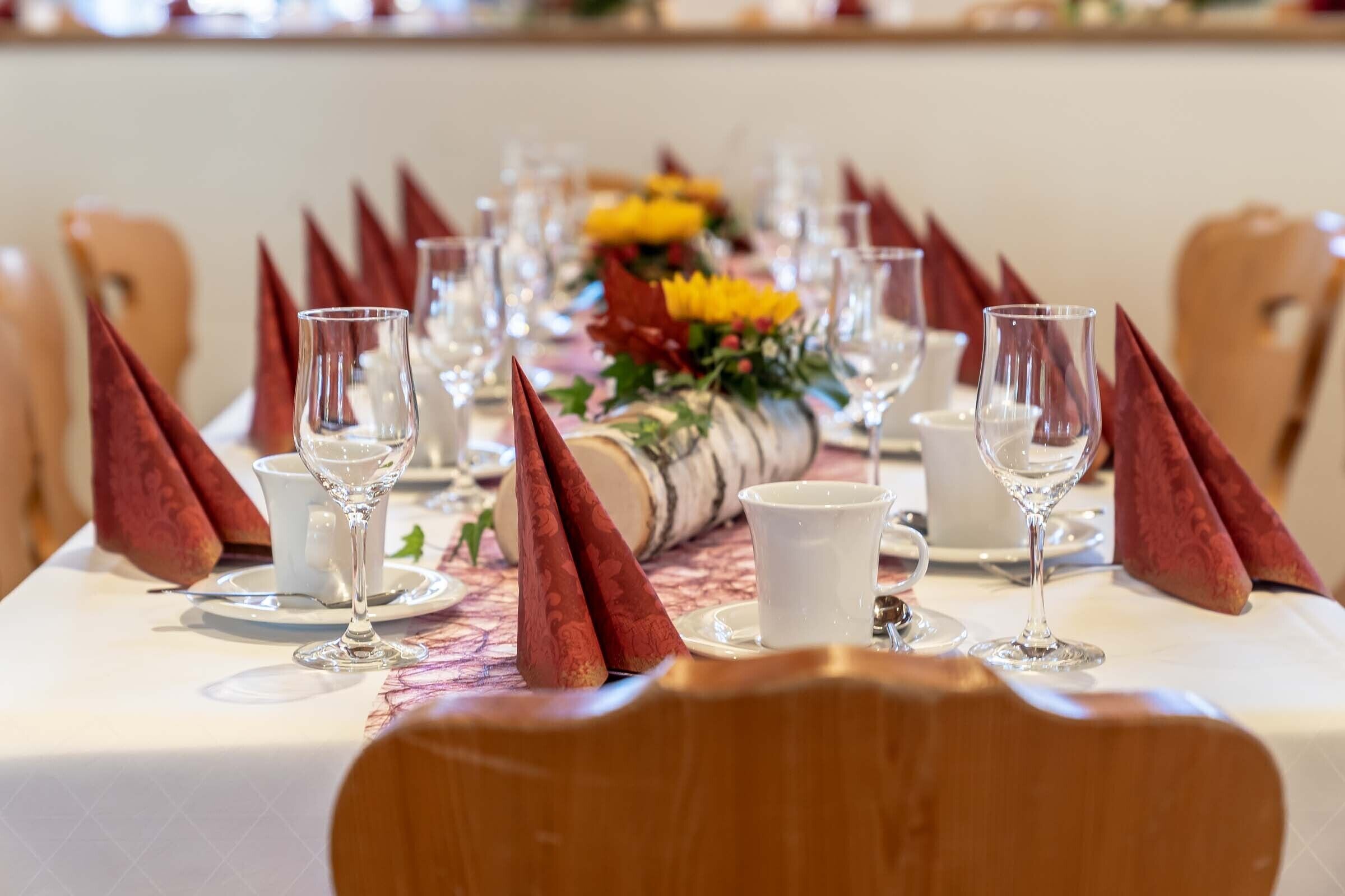 A dining table set with clear glassware, red napkins, and a centerpiece with yellow flowers.
