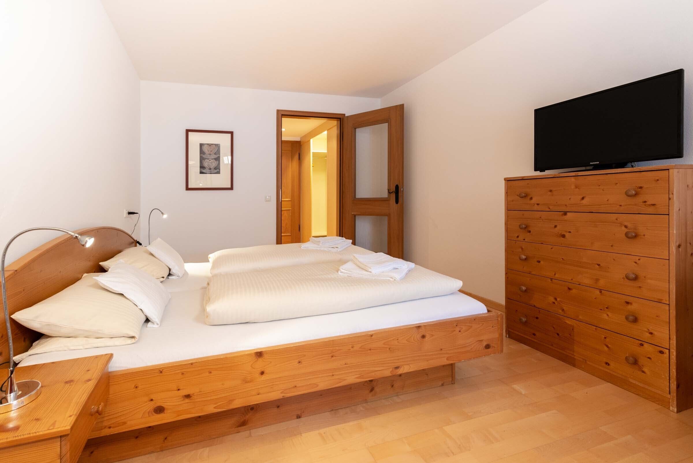 A bedroom with a wooden bed, a dresser, a television, and a framed picture on the wall.