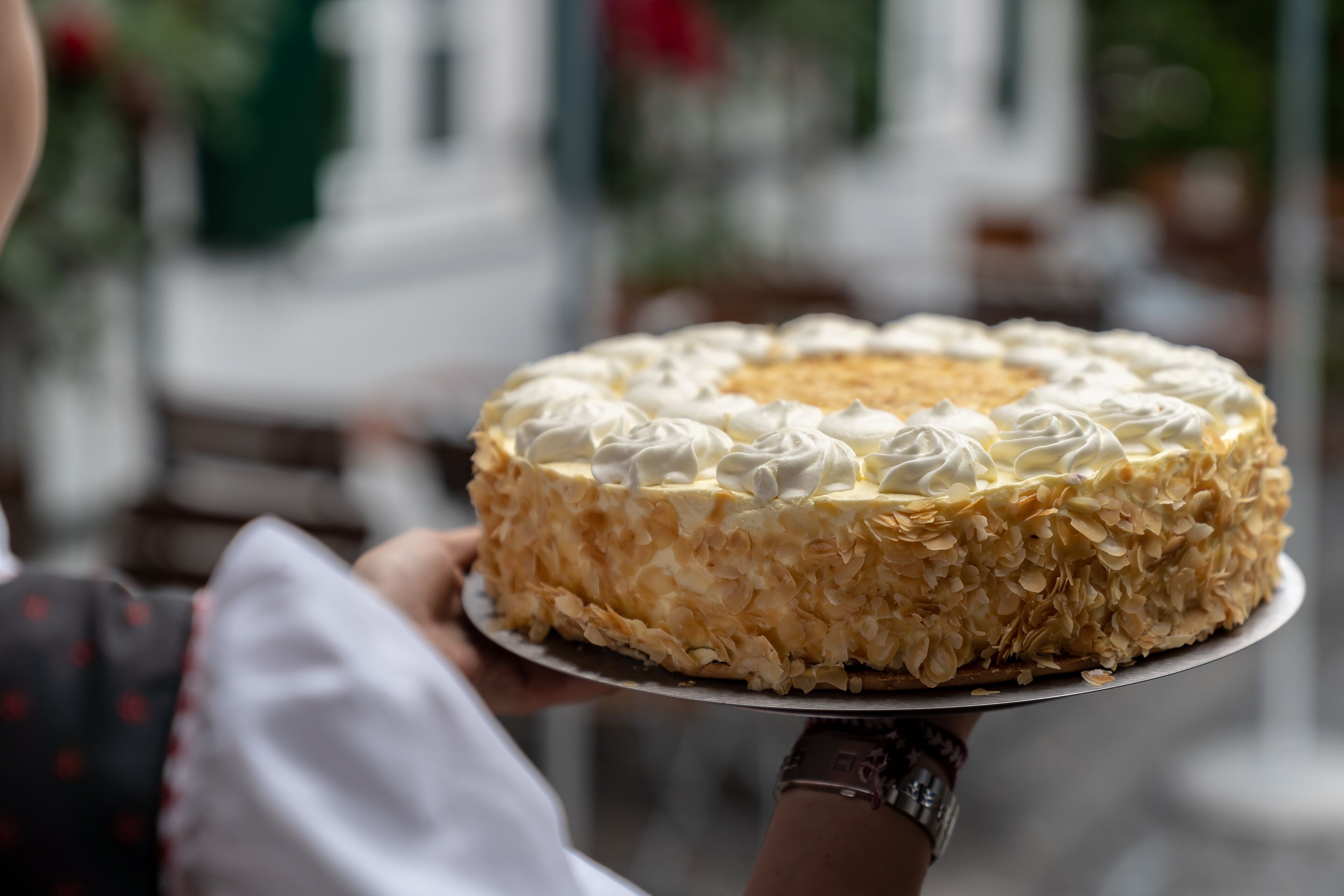 A round cake with white frosting and almond slices on a metal plate.