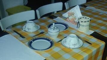 A dining area with checkered tablecloths, white chairs, and a small table with a basket and a ceramic pig figurine.