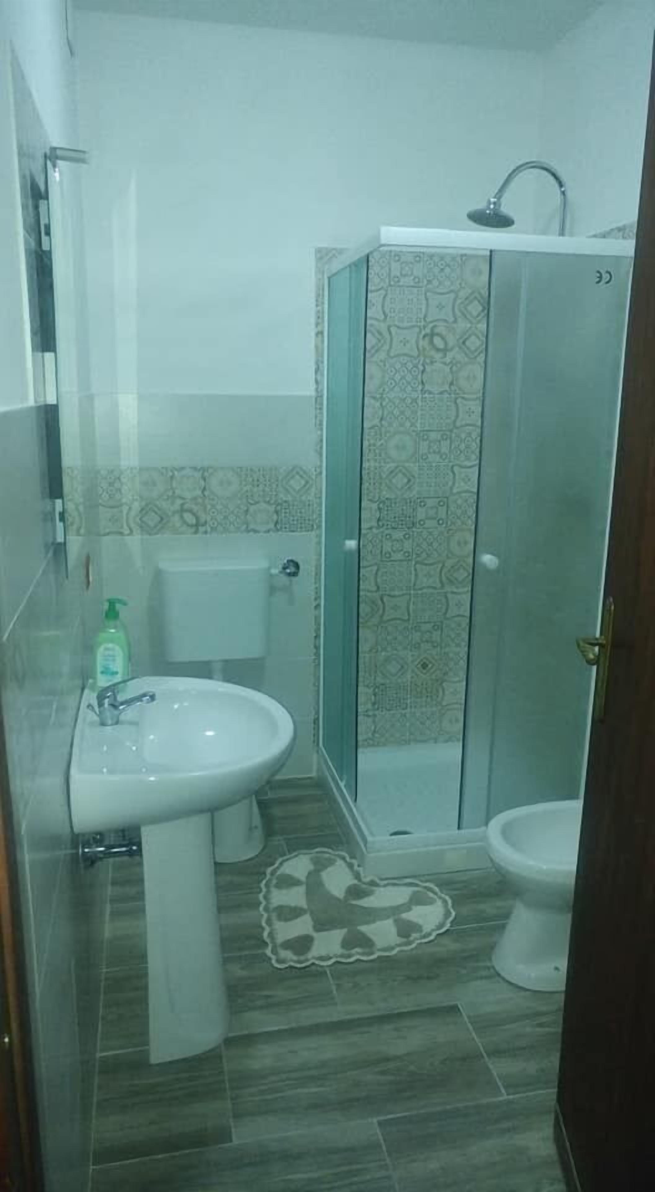 Um banheiro com chuveiro em box de vidro, pia de pedestal e vaso sanitário.