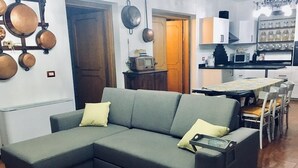 A living room with a grey sectional sofa, a coffee table, and a kitchen area with white cabinets and a microwave. - B&B Il Cedro (Foligno)