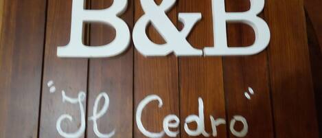 Letras de madera que deletrean “B&B” y “El Cedro” sobre una superficie de madera.