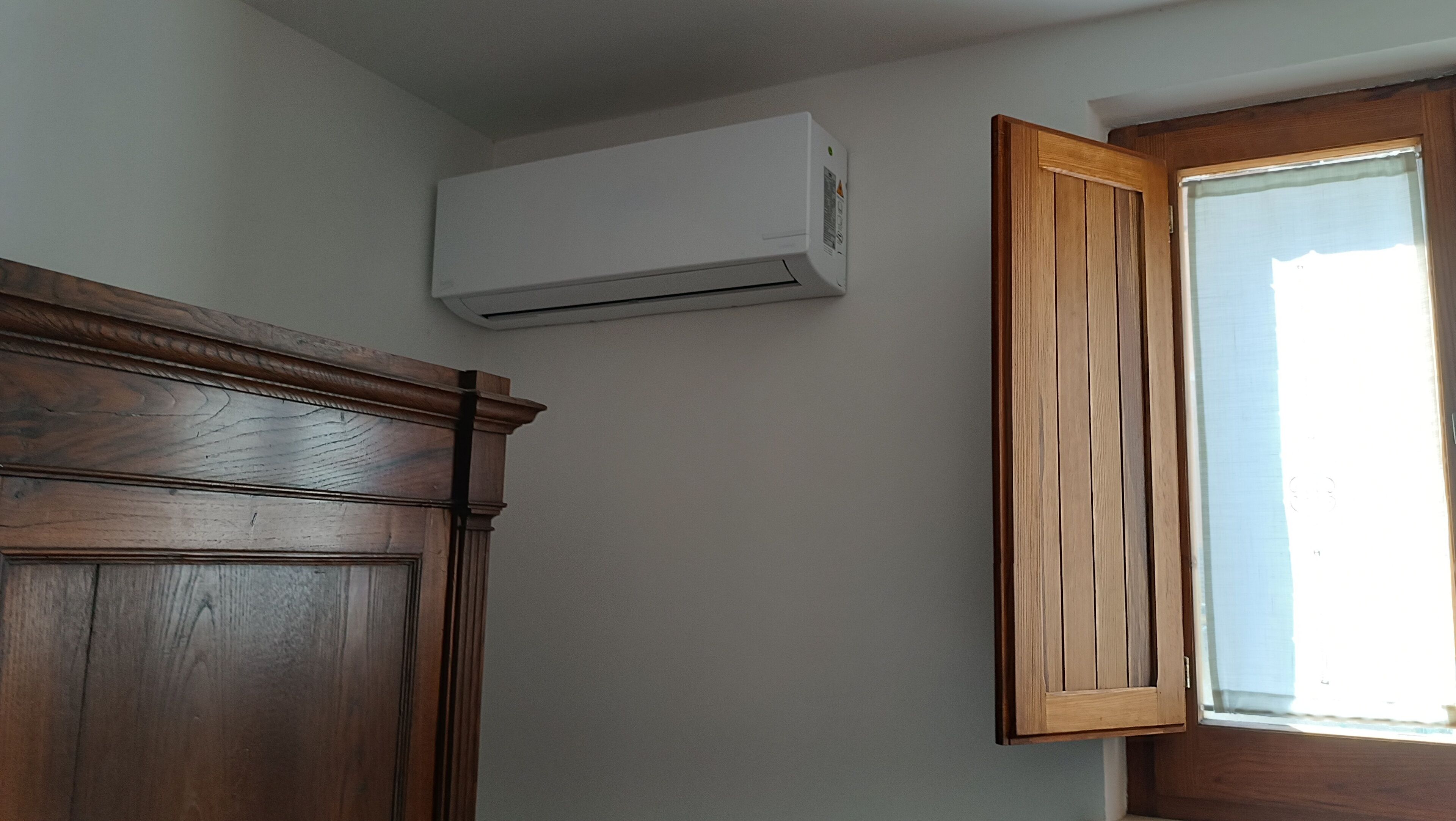 A room with a wooden cabinet, a window with a wooden frame, and a wall-mounted air conditioning unit.