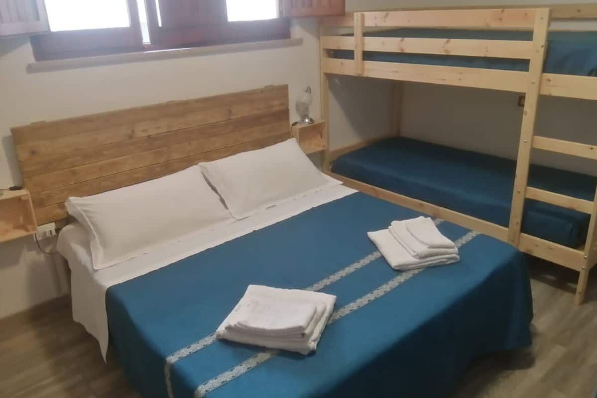 A room with a bunk bed, a single bed with a blue bedspread, and a wooden headboard.