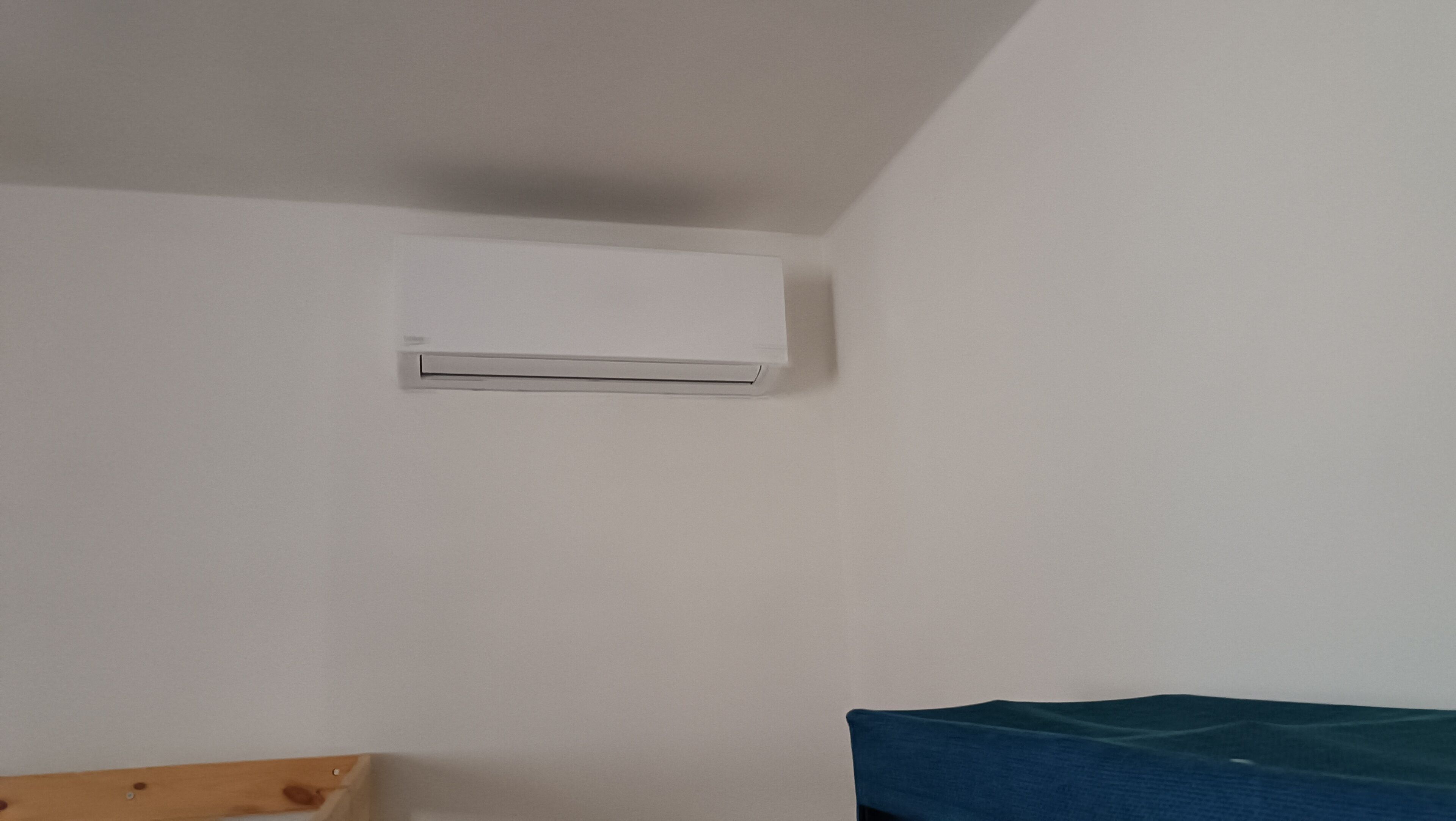 Un appareil de climatisation blanc, fixé à un mur sobre dans une pièce au mobilier réduit au minimum.