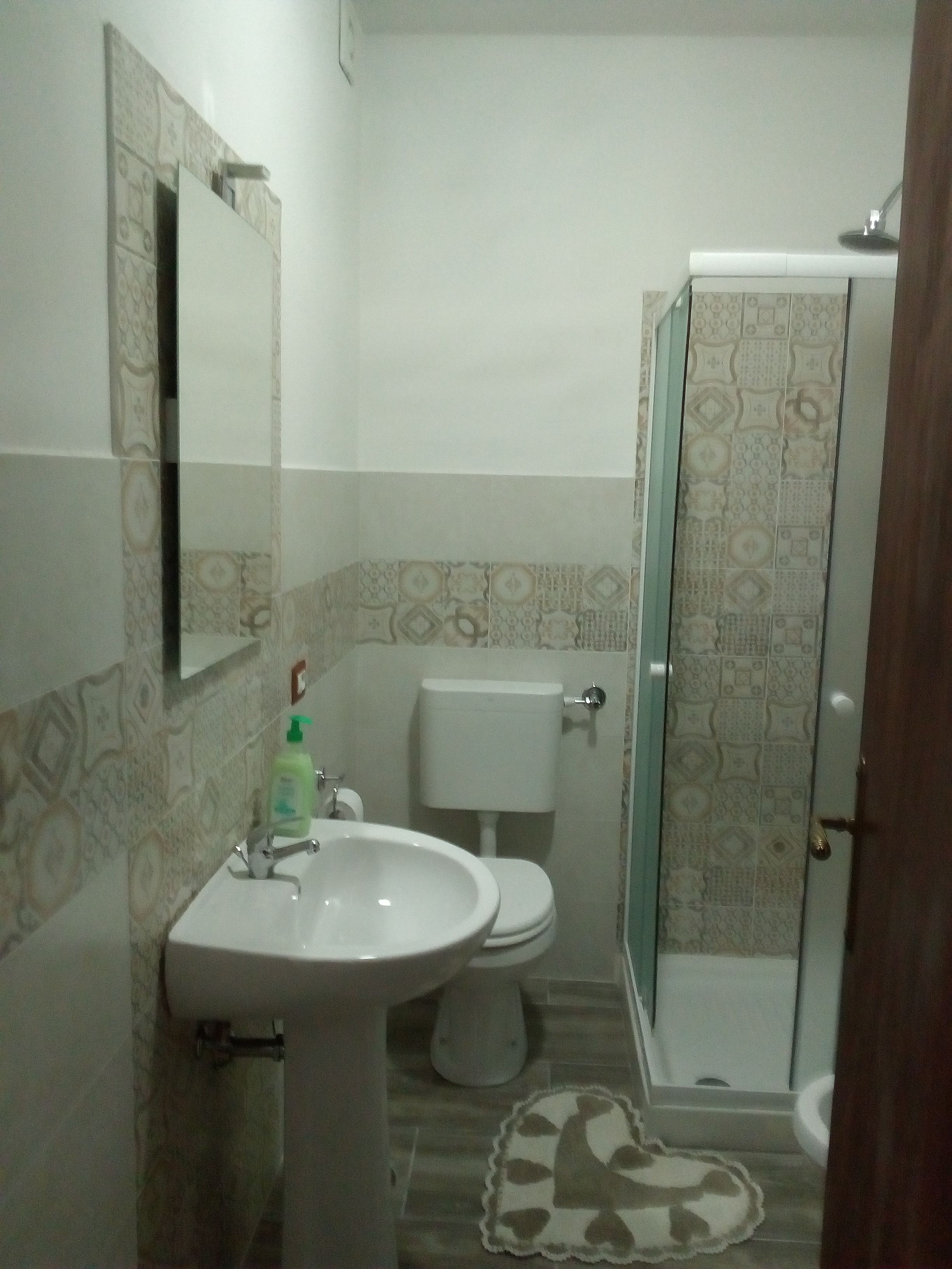 A bathroom with a white sink, toilet, and shower. The walls have patterned tiles.