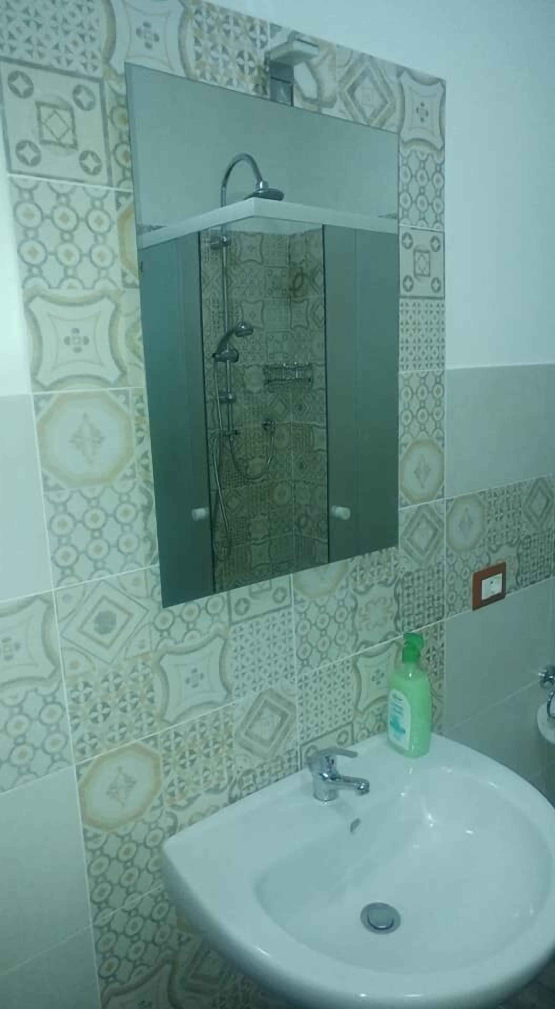 A bathroom with patterned tiles, a glass-enclosed shower, and a white sink with a green bottle.