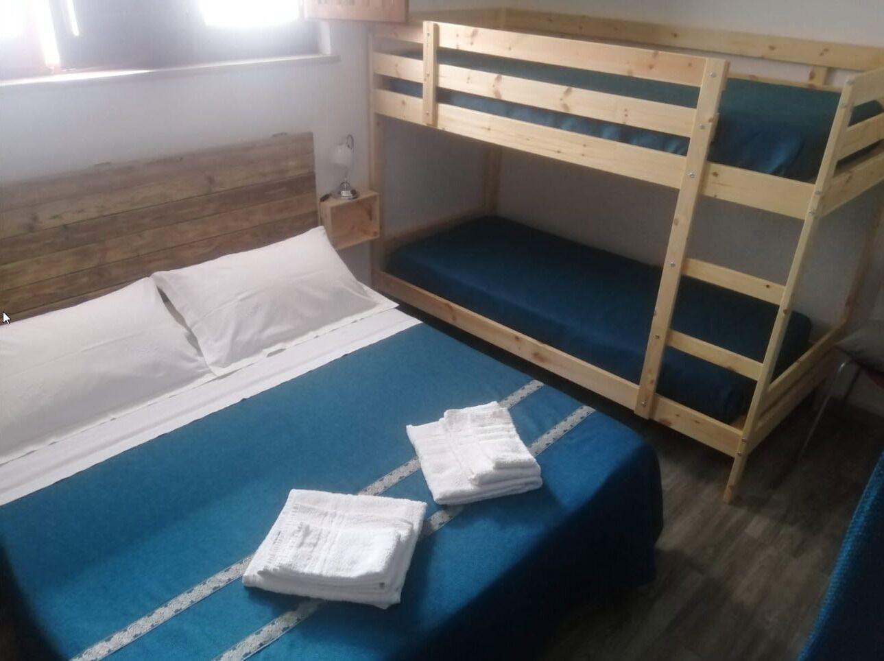 Camera con letto a castello, materasso blu, cuscini bianchi e un comodino con una lampada.