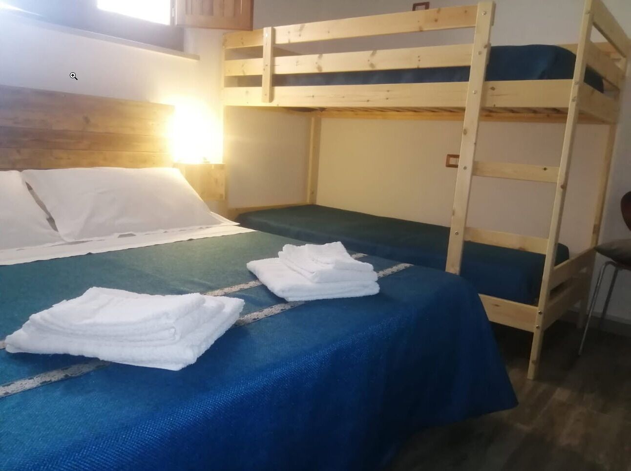 A bunk bed room with a blue bedspread, white pillows, and folded towels on the bed.