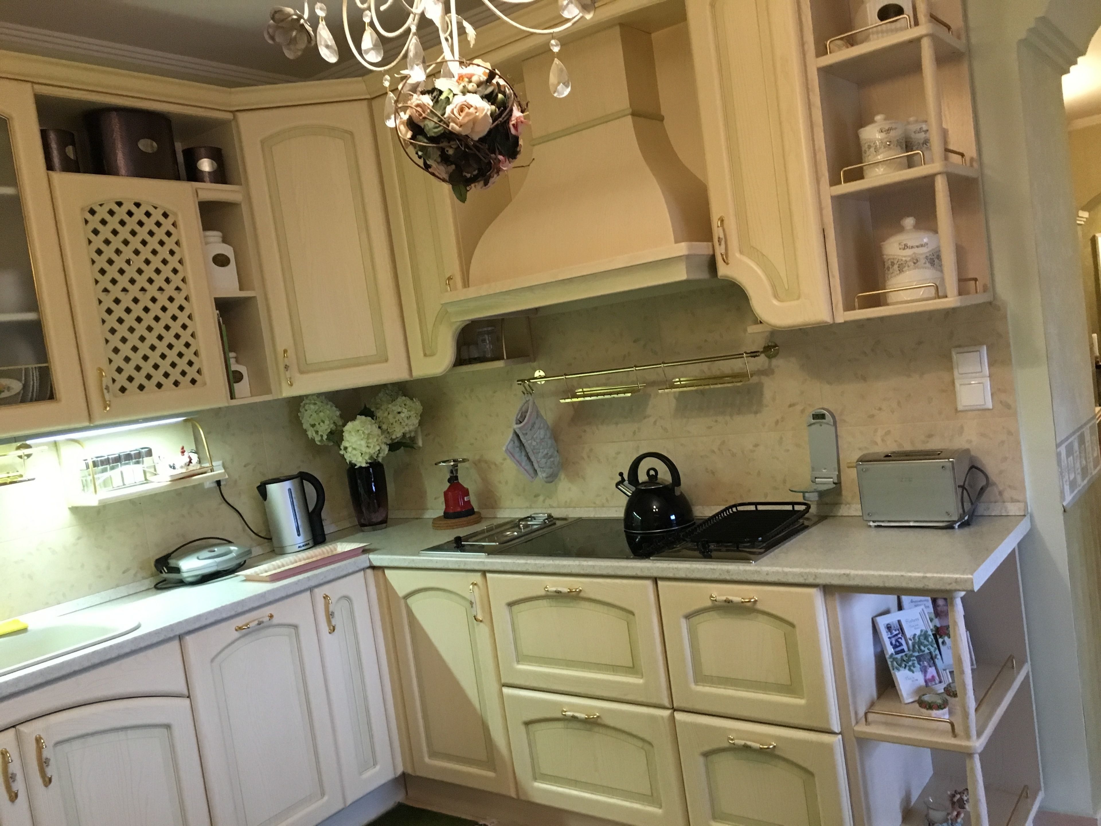 A kitchen with white cabinets, a black kettle, a toaster, and a vase with flowers.