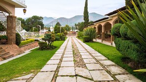A stone pathway leading to a building with a balcony and a well-maintained garden.