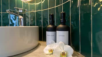 Et badeværelse med en hvid vask, to flasker mærket "HAND SOAP" og "LOTION", samt hvide orkidéer på gulvet.