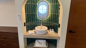 A bathroom with a round mirror, a sink, and a shelf with toiletries.