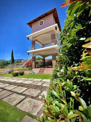 A two-story building with a balcony, stone steps, and a garden with a hedge. - Hotel Ojo de Agua (Ciudad Hidalgo)