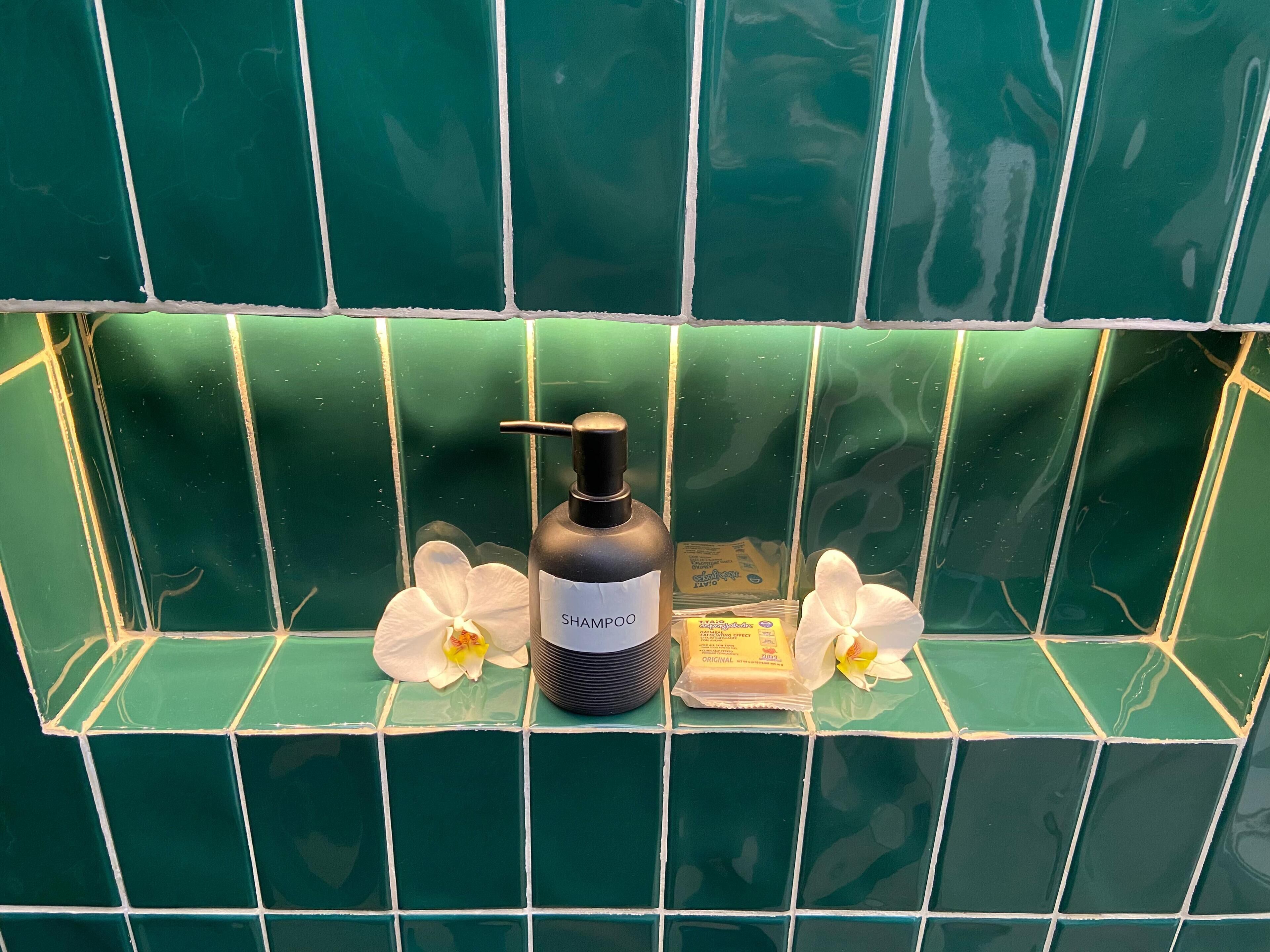 Ein Badezimmer mit grünen Fliesen, einer schwarzen Shampooflasche und zwei weißen Blumen.