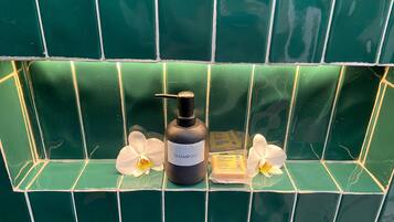 Ein Badezimmer mit grünen Fliesen, einer schwarzen Shampooflasche und zwei weißen Blumen.