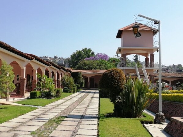A building with a covered walkway, a bell tower, and a garden with neatly trimmed hedges. - Hotel Ojo de Agua (Ciudad Hidalgo)