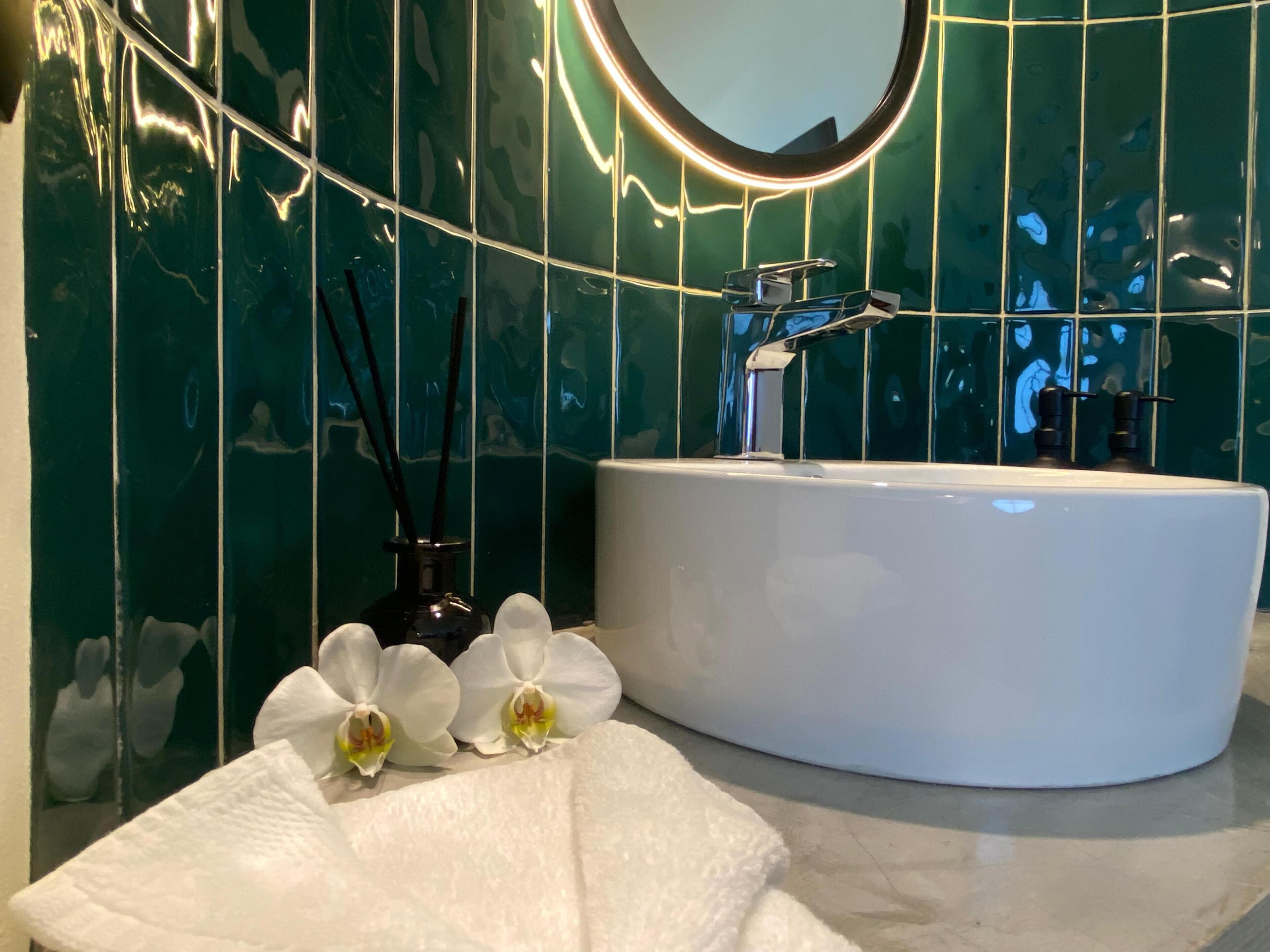A bathroom with a white sink, a mirror, and green tiled walls.
