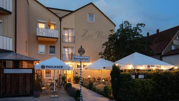 Ein Hotel namens 'Zur Post' mit Außenbestuhlung und Sonnenschirmen, einem Schild für 'Biergarten' und einem Paulaner-Bierzelteinrichtung.