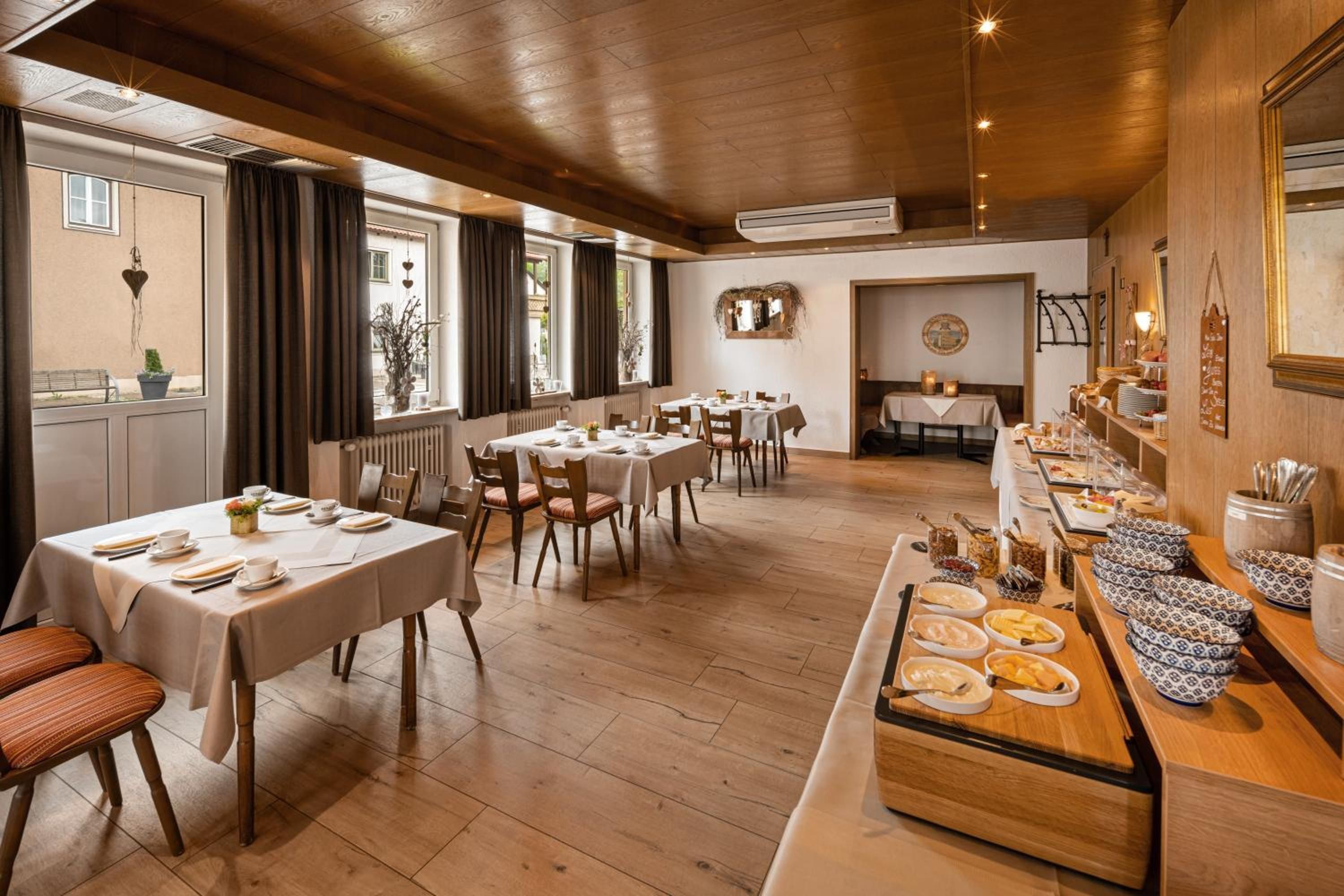 Ein Restaurant mit mehreren Tischen, einem Buffet und Blick ins Freie.