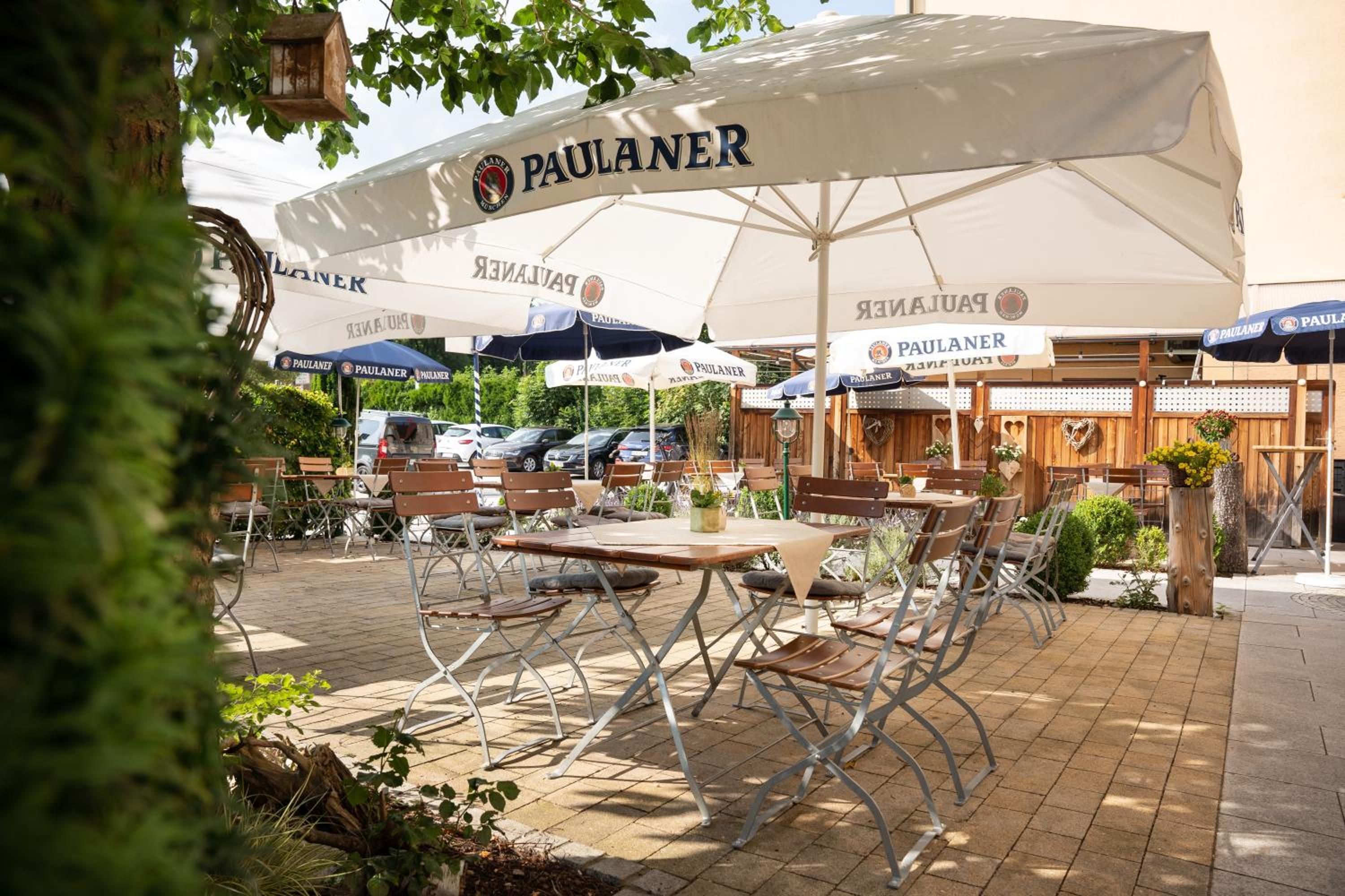 Ein Außenbereich mit Tischen und Stühlen unter Sonnenschirmen mit dem Schriftzug 'PAULANER'.