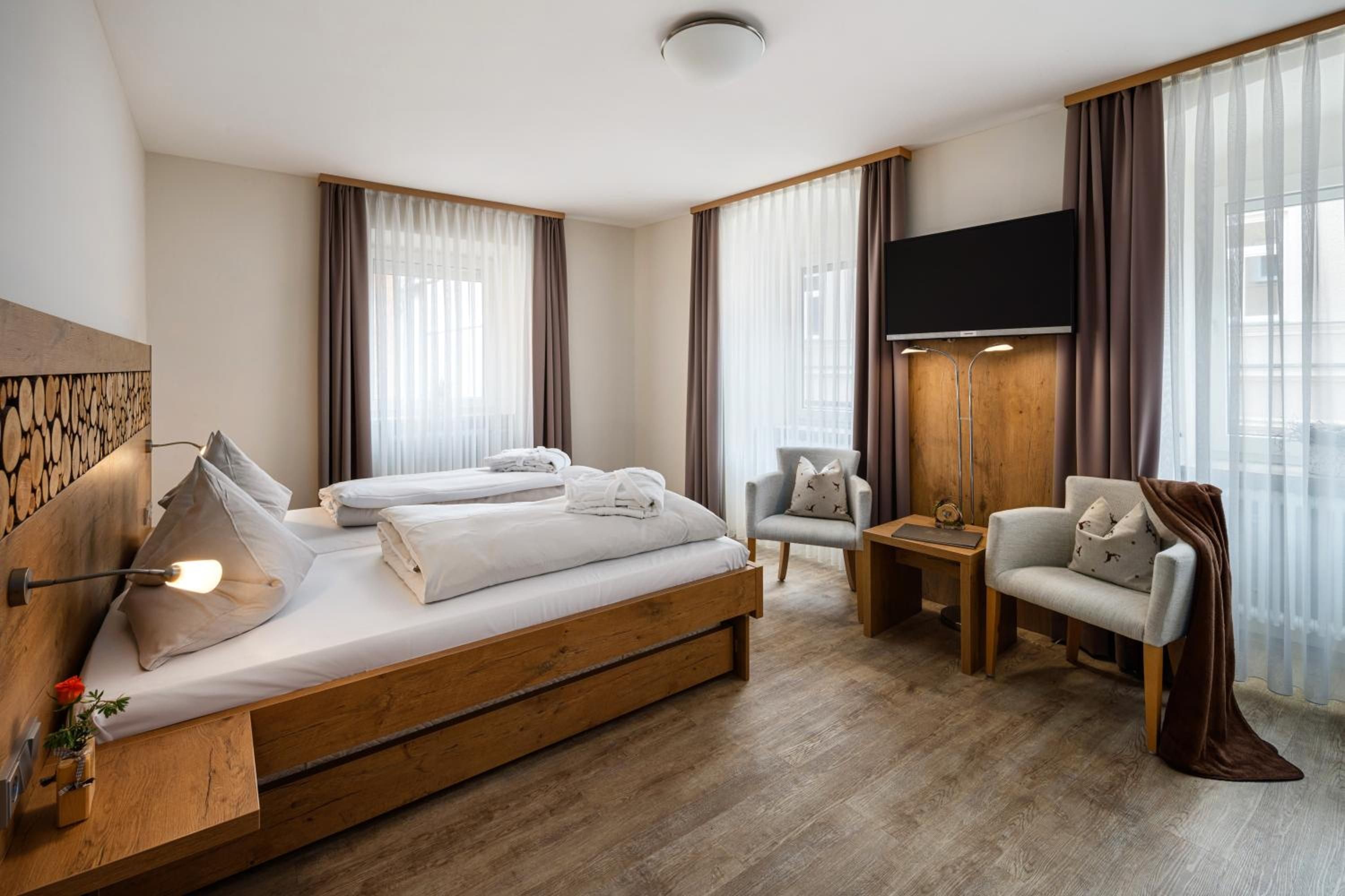 Ein modernes Hotelzimmer mit einem großen Bett, einem Schreibtisch, einem Sessel und einem Fernseher.