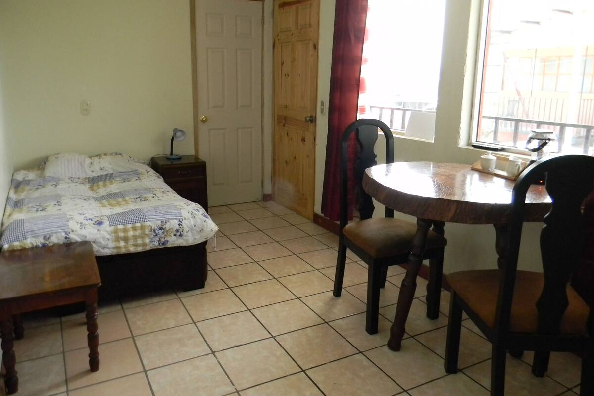A room with a bed, a small table with chairs, a window with a view, and a door.
