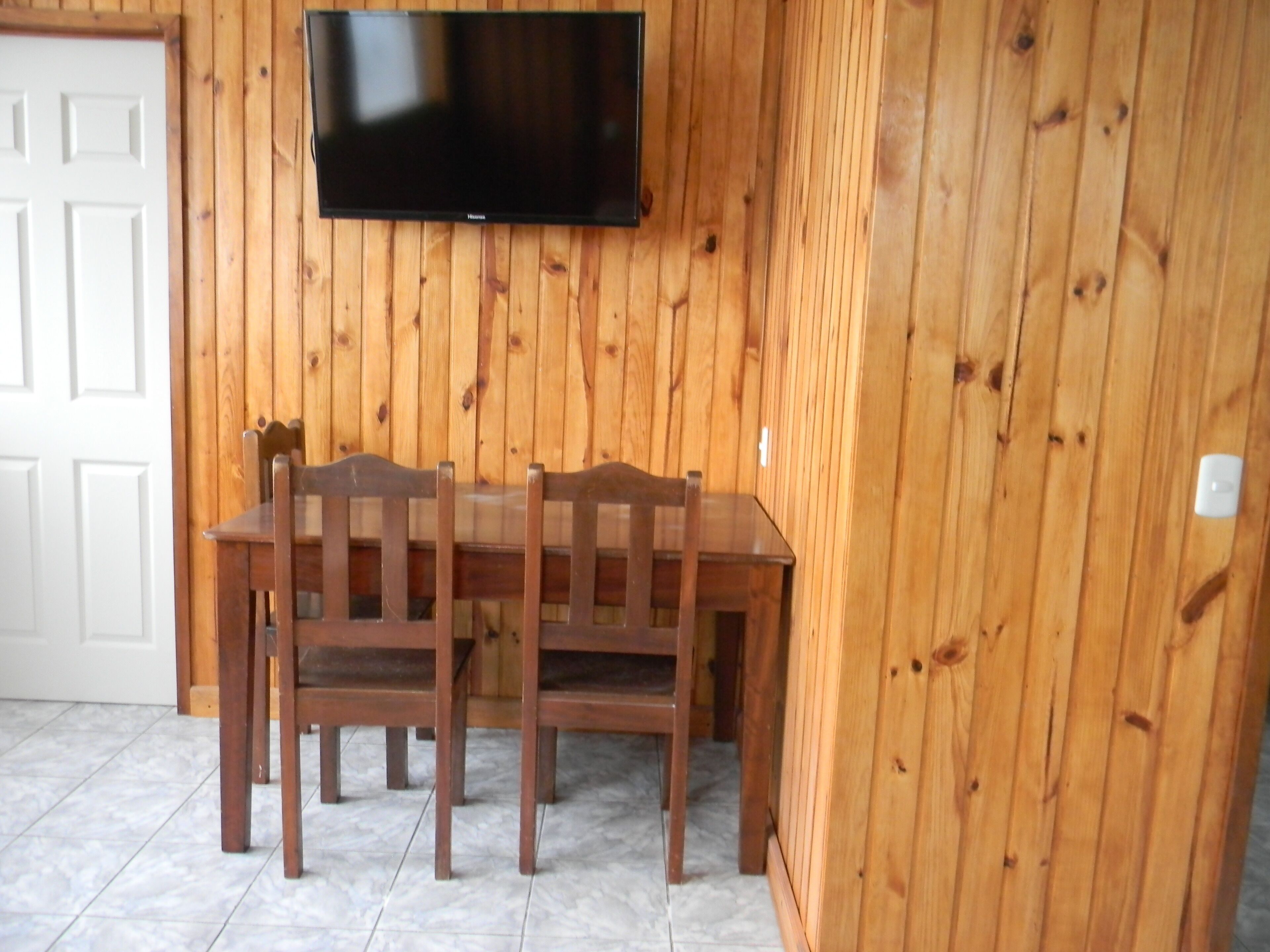 A wooden-paneled room with a TV mounted on the wall, a wooden table, and four chairs.