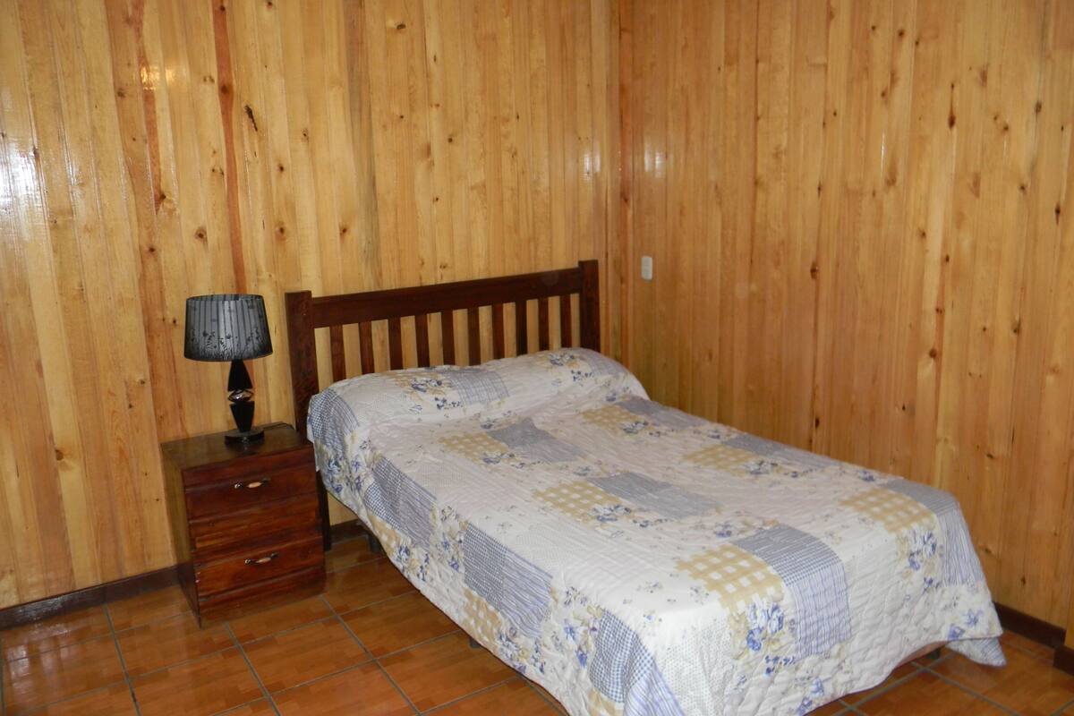 A bedroom with a wooden headboard, a bed with a floral quilt, a nightstand with a lamp, and a wooden dresser.
