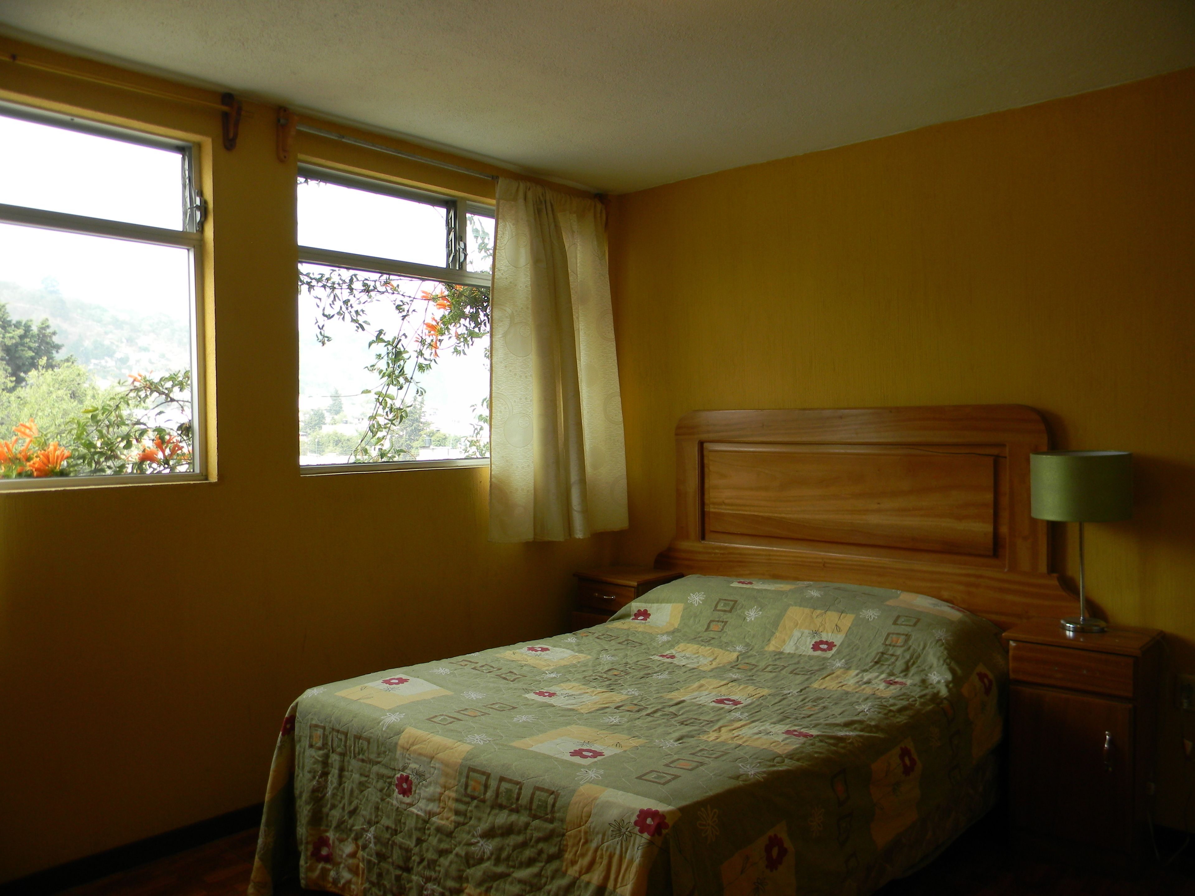 A bedroom with a bed, a nightstand, a lamp, and a window with curtains.
