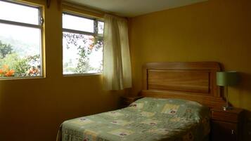 A bedroom with a bed, a nightstand, a lamp, and a window with curtains.