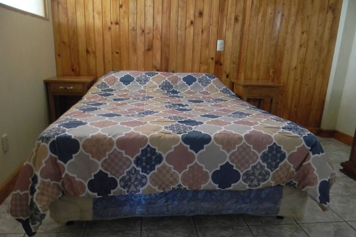 A bed with a patterned bedspread in a room with wooden paneling on the walls.