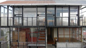 Un bâtiment moderne à deux étages, doté de grandes fenêtres, d’un escalier et d’un petit espace extérieur aménagé en coin salon.