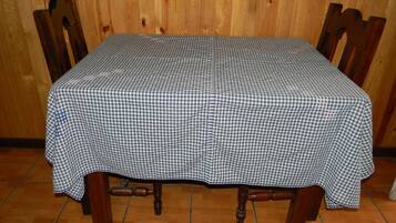 Uma mesa com toalha xadrez, cadeiras de madeira e um fundo de parede de madeira.