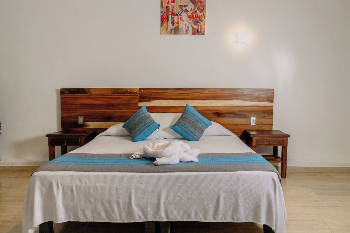 Una cama bien tendida con cabecera de madera, dos almohadas y una manta.